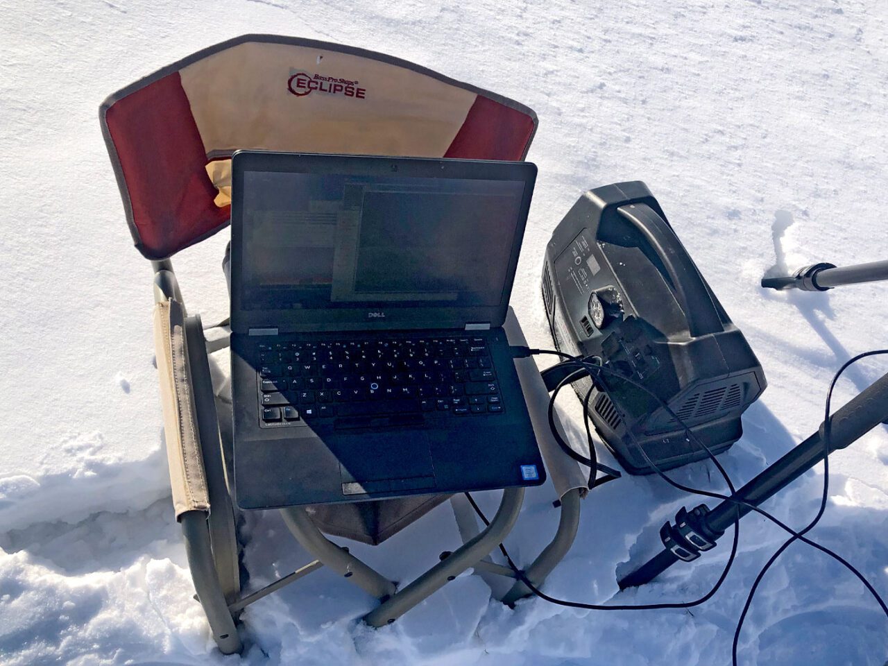 A chair with a computer on the seat, connected to some kind of box.