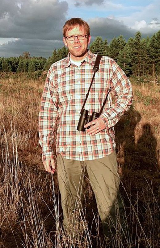 Man stands in field with binoculars.