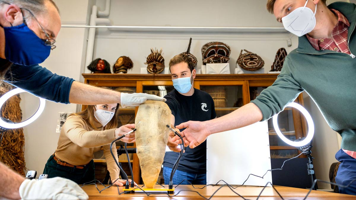 Four people wearing gloves and masks attach scanning equipment to a brown bundle containing a mummified ibis.